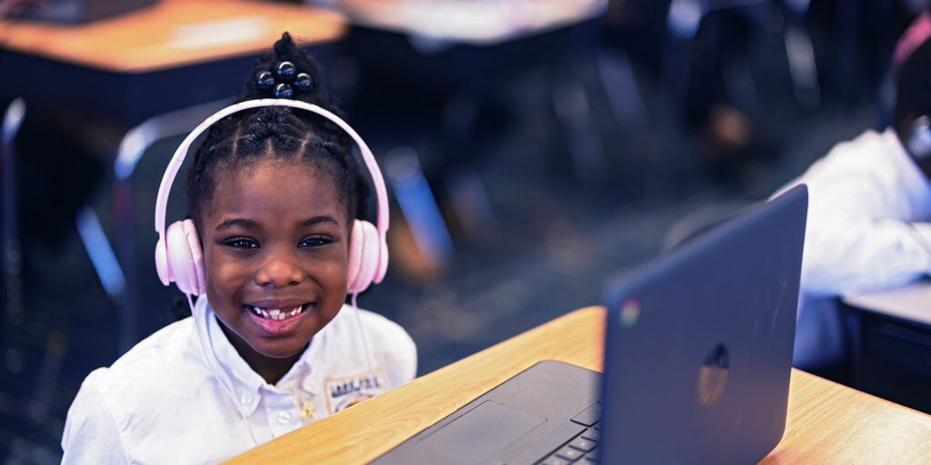student at a desk smiling while wearing a headset